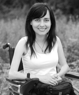 A black and white photo of a fair-skinned young woman with dark hair sitting in a wheelchair with a field behind her.